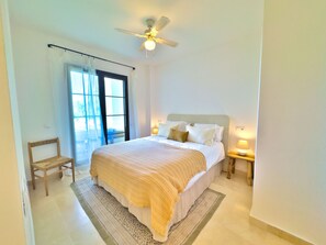 A bedroom with a bed, a chair, a nightstand, a ceiling fan, and a window with curtains. - Sea View Golf Retreat. Los Arqueros Benahavís (Benahavís)