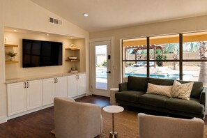 A modern living room with a flat-screen TV, white cabinets, a green sofa, and a view of a swimming pool. - Saltwater Pool, Walk to Pickleball, North Phoenix Retreat,  Norterra Shopping. (Phoenix)