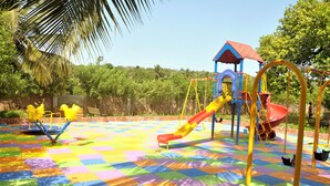 Un patio de juegos con piso a cuadros de colores, un tobogán, columpios y una estructura para escalar.