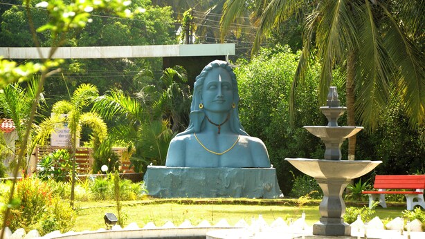 Una estatua en un jardín con una fuente y un banco.