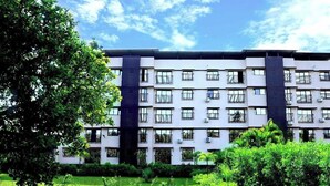Un edificio de varios pisos con balcones, rodeado de abundante vegetación.