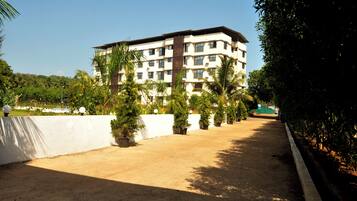 A multi-story building with a flat roof, surrounded by a landscaped area with palm trees and a white wall.