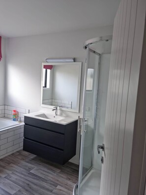 Ein modernes Badezimmer mit einem weißen Waschbecken, einem dunklen Waschtisch und einer Duschkabine aus Glas.