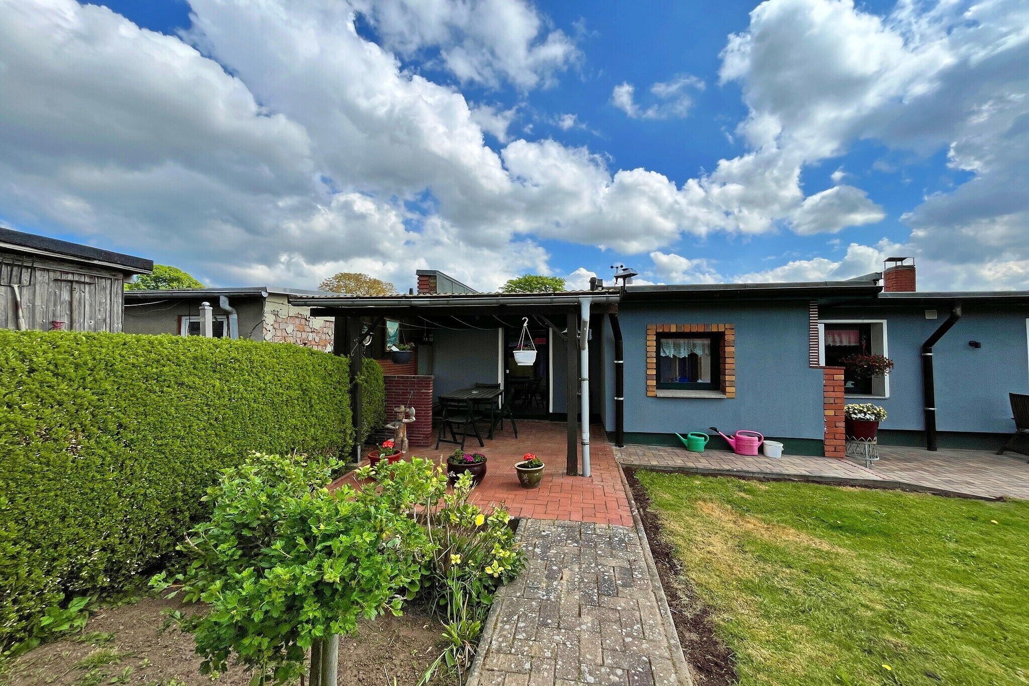 Ein Wohnhaus mit überdachter Terrasse, einem gepflasterten Weg und einem gepflegten Garten.