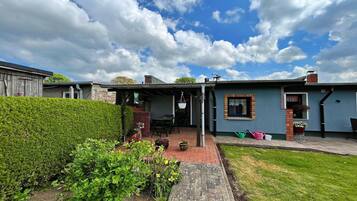 Ein Wohnhaus mit überdachter Terrasse, einem gepflasterten Weg und einem gepflegten Garten.