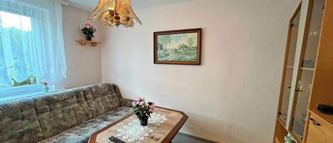 A living room with a sofa, a table with a remote control, a chandelier, a framed picture, and a cabinet.