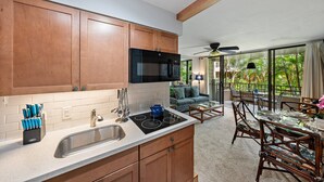 A kitchen with wooden cabinets, a black microwave, and a blue kettle on the countertop. - 1BR Condo Near Oceanfront Lawn, Pool & Sunset Views- Paki Maui 212 (Lahaina)