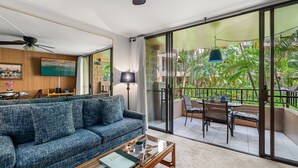 A living room with a sofa, coffee table, and a balcony with outdoor furniture. - 1BR Condo Near Oceanfront Lawn, Pool & Sunset Views- Paki Maui 212 (Lahaina)