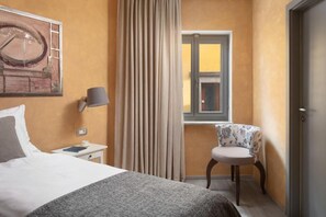 Ein Hotelzimmer mit Bett, Stuhl, Lampe, Fenster und Tür.