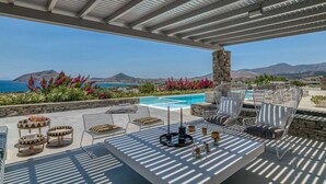 Um pátio externo com piscina, espreguiçadeiras e vista para o mar e as montanhas.