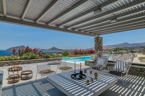 An outdoor patio with a pool, lounge chairs, and a view of the sea and mountains. - Villa La Magnifique - The best view (Naousa)