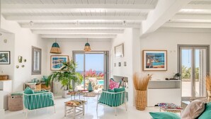 Uma sala de estar espaçosa com vista para o mar, uma varanda e um espaço de jantar com mesa e cadeiras.