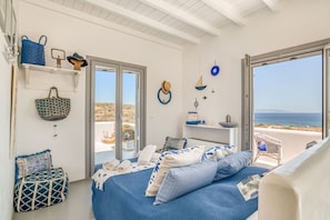 A bedroom with a bed, a chair, a shelf with decorative items, and a view of the sea. - Villa La Magnifique - The best view (Naousa)