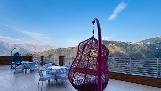 A terrace with a table and chairs, a hanging chair, and a view of mountains.