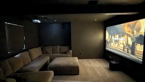 Una habitación oscura con una pantalla grande mostrando una película, un sofá y un sillón reclinable.