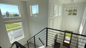 Una habitación amplia con techo alto, ventanas grandes y una escalera con barandilla negra.