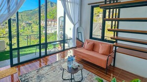 Una sala de estar moderna con sofá, mesa de centro y ventanas amplias que dan a un paisaje verde.