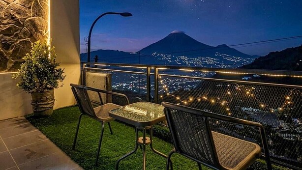 Una terraza con vistas a una montaña y la Vía Láctea, amueblada con sillas y una mesa.