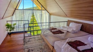 Un dormitorio con techo inclinado, un ventanal y vistas a la vegetación.