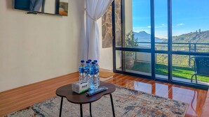 Una habitación con un ventanal grande, un televisor de pantalla plana, una pequeña mesa con botellas de agua y una alfombra estampada.