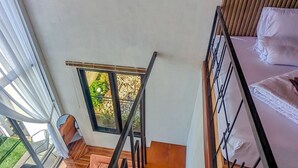 Una escalera de madera con barandillas metálicas que lleva a un dormitorio con cama y ventana.