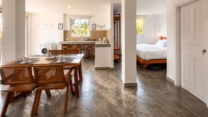 A modern hotel room with a wooden dining table, chairs, a kitchen area, and a bed. - Samsara - Villa Cappucino (Koh Rong)