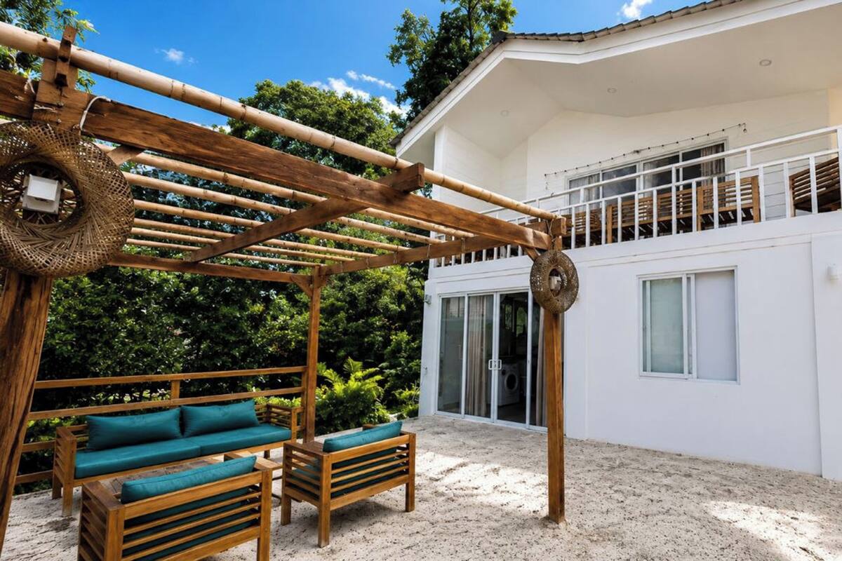 Una casa moderna con una pérgola de madera, mobiliario exterior y un balcón.