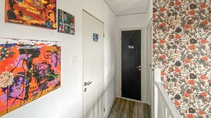 Käytävä, jossa on puulattia, ovi, jonka yläpuolella on kyltti, jossa lukee ”WC”, ja seinät on koristeltu värikkäillä taideteoksilla.