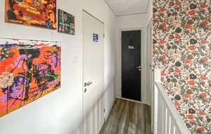 Un couloir doté d’un plancher en bois, une porte portant l’inscription « TOA », et des murs décorés d’œuvres d’art colorées.