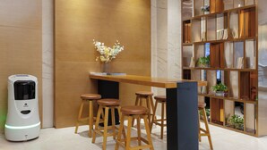 A modern bar area with a wooden counter, bar stools, a decorative plant, and a bookshelf with books and plants. - Yasite Hotel Yuyuan Road Metro Station (Kunming)