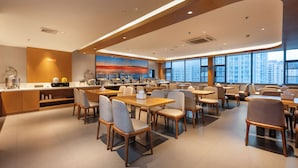A modern dining area with multiple tables and chairs, a kitchen counter, and large windows offering a city view. - Yasite Hotel Yuyuan Road Metro Station (Kunming)