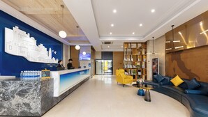 A hotel lobby with a reception desk, a blue sofa, a coffee table, and a bookshelf. - Yasite Hotel Yuyuan Road Metro Station (Kunming)
