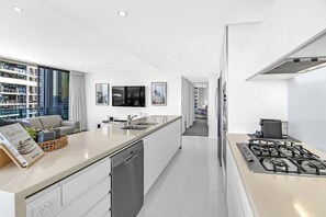 A modern kitchen with a central island, built-in dishwasher, and a gas stove. - Ocean Sunrise at Oracle Level 9 (Gold Coast City)