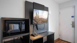 A room with a television mounted on a wall, a microwave on a counter, and a door with a sign. - 2 Queen Beds | Smoking (Chandler)