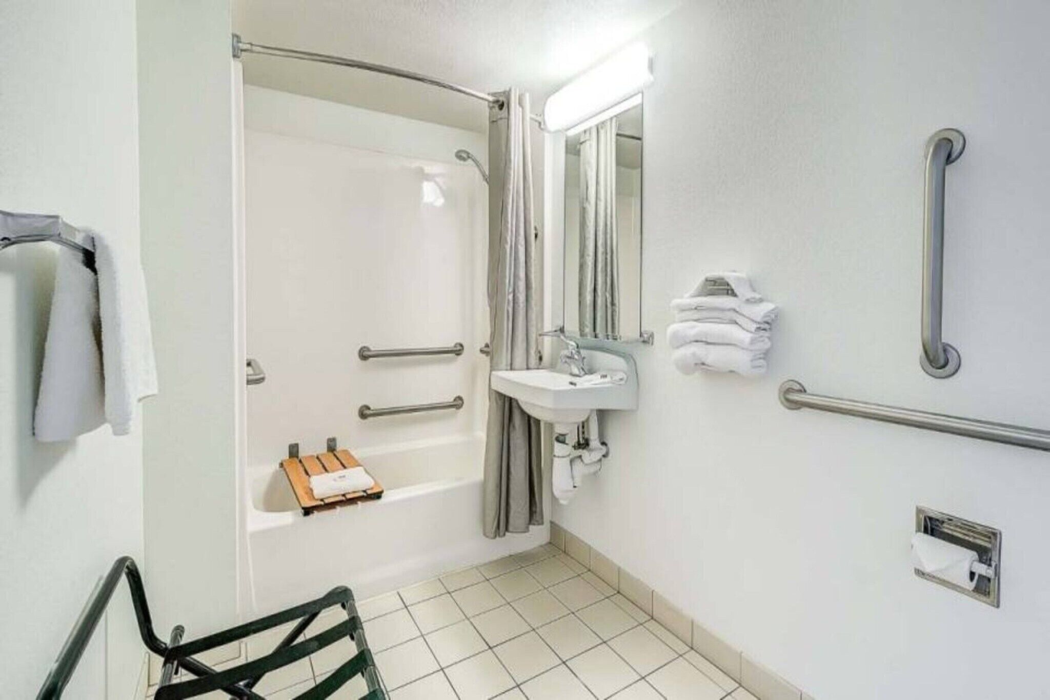 Ein Badezimmer mit Dusche, Waschbecken, Spiegel und Haltegriffen.