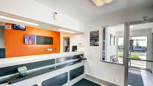 A reception area with a counter, a digital scale, a large orange sign with the number 6, and a glass door leading outside. - 1 Full Bed|Mobility Access Tub| NS (Thornton)