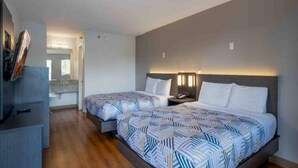 Habitación de hotel con dos camas, un escritorio y un baño visible a través de una puerta abierta.