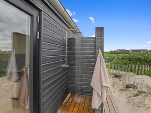 Eine Holzterrasse mit einer Duschkabine und einem Handtuch, das an der Reling hängt.