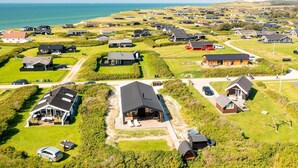 Une vue aérienne d’une zone résidentielle côtière, avec des maisons, une plage et un ciel dégagé.