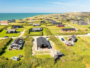 Luftaufnahme einer Küstenwohngegend mit Häusern, einem Strand und blauem Himmel.