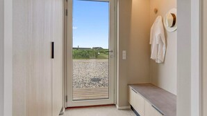 Un couloir avec une porte donnant sur un balcon dont le sol est recouvert de gravier et qui offre une vue sur un ciel dégagé.