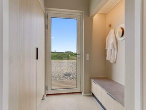 Ein Flur mit einer Tür, die auf einen Balkon mit Kiesboden und blauem Himmel führt.