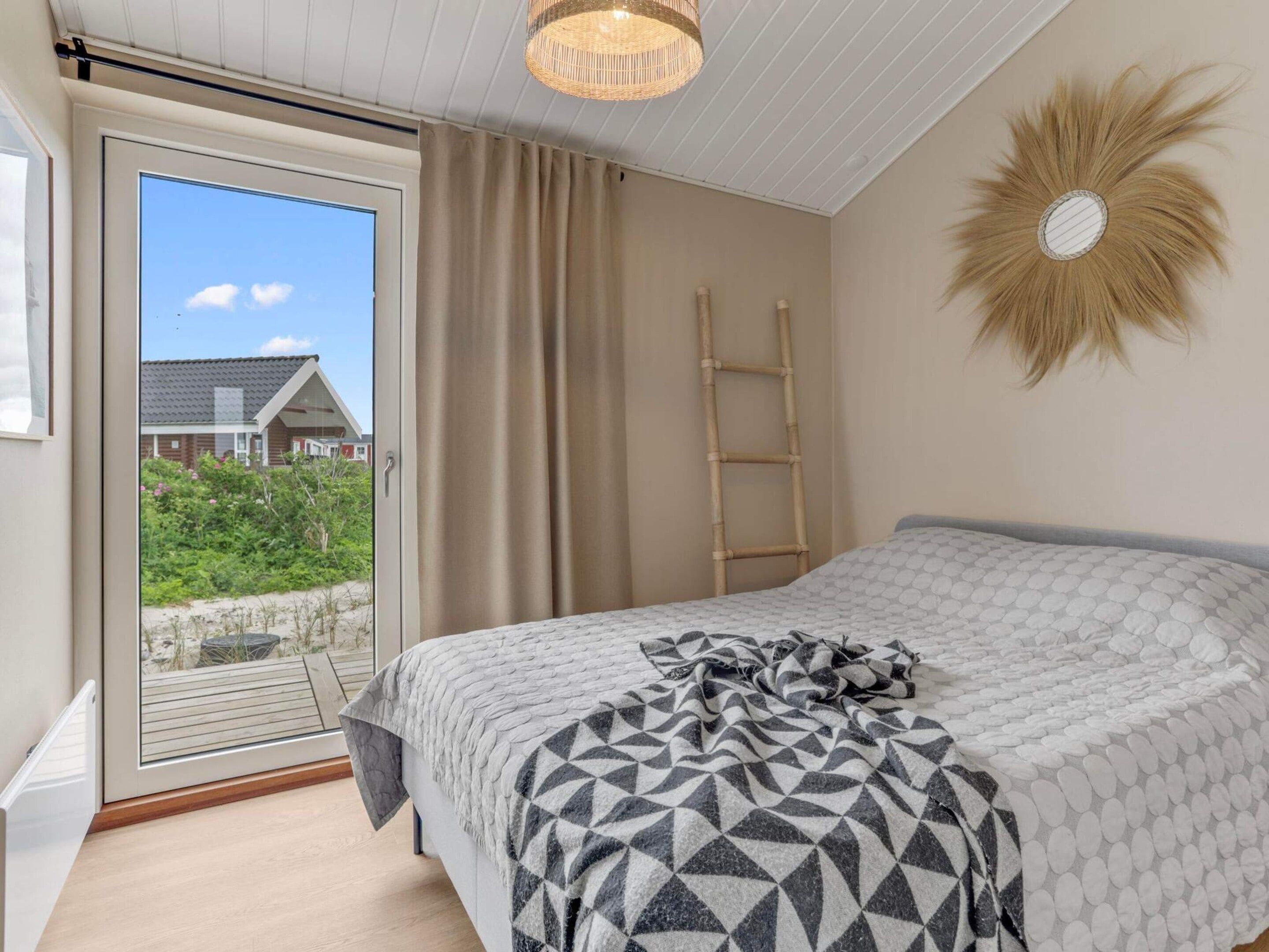 A bedroom with a bed, a window with curtains, a view of a house, and a wall-mounted decorative item.