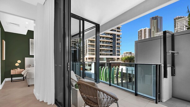 Een balkon met een stoel, een bed en uitzicht op hoogbouw.