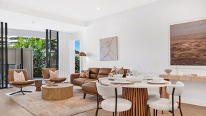 Een moderne woonkamer met een ronde houten eettafel, leren banken en een groot raam met uitzicht op groen.