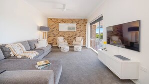 Un salon moderne avec un canapé gris, deux fauteuils, un téléviseur à écran plat et un mur décoratif en briques.