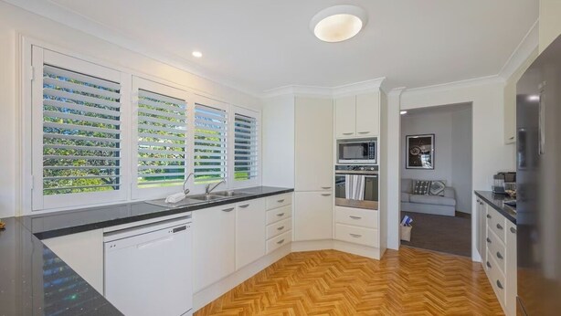Une cuisine moderne avec des meubles blancs, un plan de travail noir et un parquet en bois disposé en chevrons.