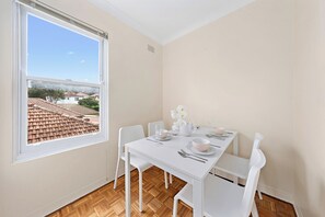Ein Essbereich mit Tisch für vier Personen, weißen Stühlen, einem Fenster mit Blick auf eine Wohngegend und einem Deckenlüfter.