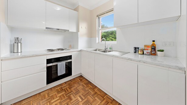 Een moderne keuken met witte kasten, een roestvrijstalen spoelbak, een ingebouwde oven en een raam met uitzicht op groen.