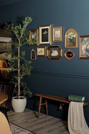 A room with a dark blue wall, a potted plant, a wooden bench, and various framed artworks.
